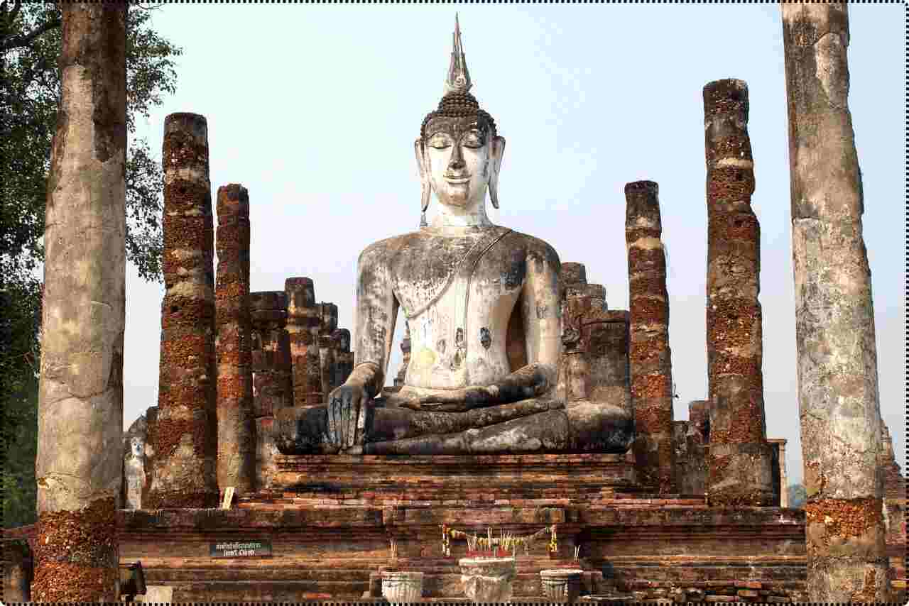 Ancient Buddha statue at Sukhothai Historical Park,surrounded by tall stone pillars.